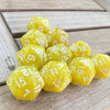 A collection of ten yellow pearl acrylic D20 dice scattered on a wooden surface.