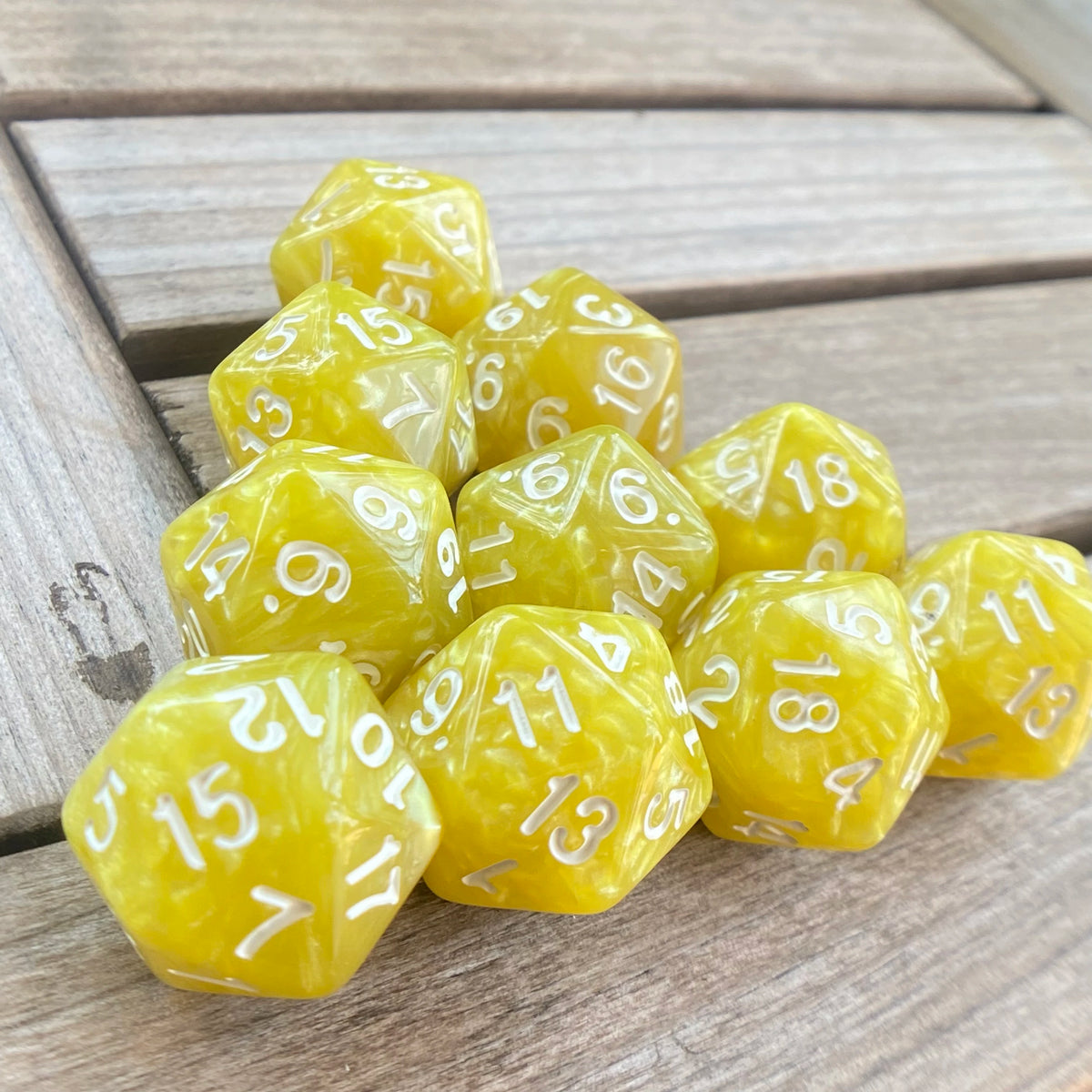 A collection of ten yellow pearl acrylic D20 dice scattered on a wooden surface.