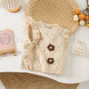 A beige knit sweater vest with a flower shape detail and ruffled edge resting on a white surface.