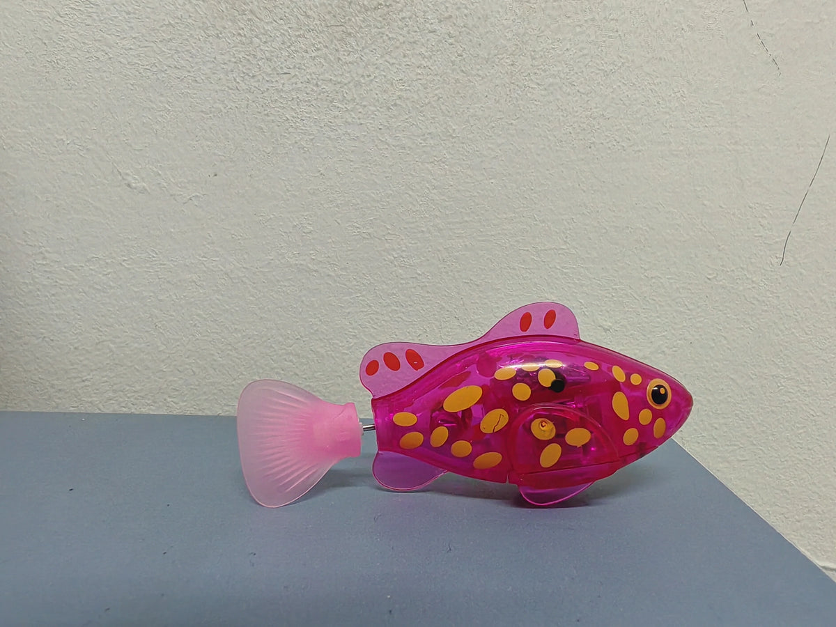 A pink light-up bath toy shaped like a fish with yellow polka dots resting on a gray surface.