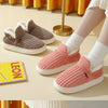 A pair of pink ribbed faux fur slippers and a pair of taupe suede slippers are displayed on a light table.
