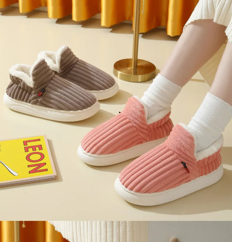 A pair of pink ribbed faux fur slippers and a pair of taupe suede slippers are displayed on a light table.
