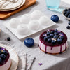 A plate of blueberries and a purple frosted cake with blueberries on top, set on a gray tablecloth.