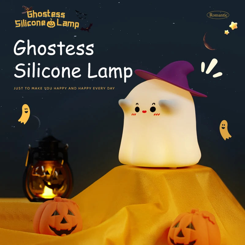 A white ghost-shaped silicone lamp sits on a yellow fabric next to carved pumpkins.