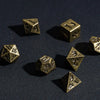 A set of small brass metal dice, including a d10 and d6, resting on a dark surface.