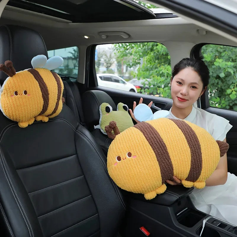 A woman in a car is holding two yellow plush animal pillows, one resembling a bee and another like a frog.
