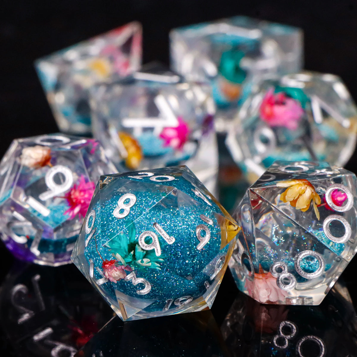A close-up of a set of handmade resin sharp edge dice in various colors and shapes resting on a reflective surface.