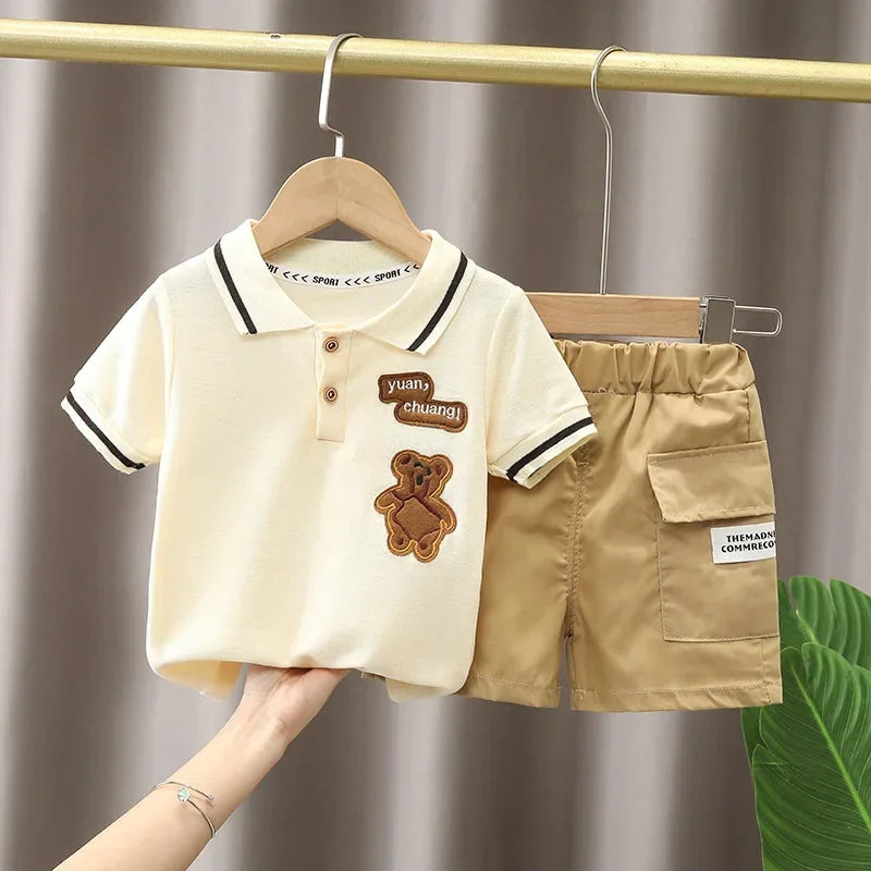 A beige boys' cotton summer short sleeve t-shirt and shorts set hanging on a wooden hanger.