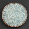 A pile of light blue to translucent aquamarine chips in a shallow brown dish.