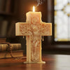 A pink floral cross candle with a lit wick sits on a wooden surface.