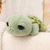 A soft, light green plush toy of a sea turtle or tortoise with large eyes resting on a white fabric.