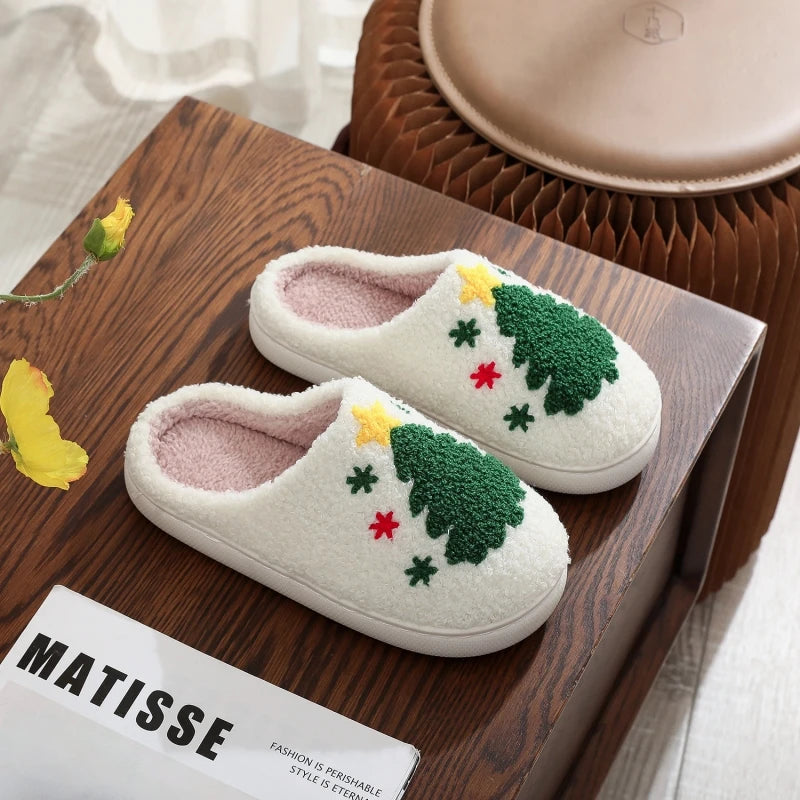 A pair of white plush indoor slippers with green and red floral embroidery resting on a wooden tray.