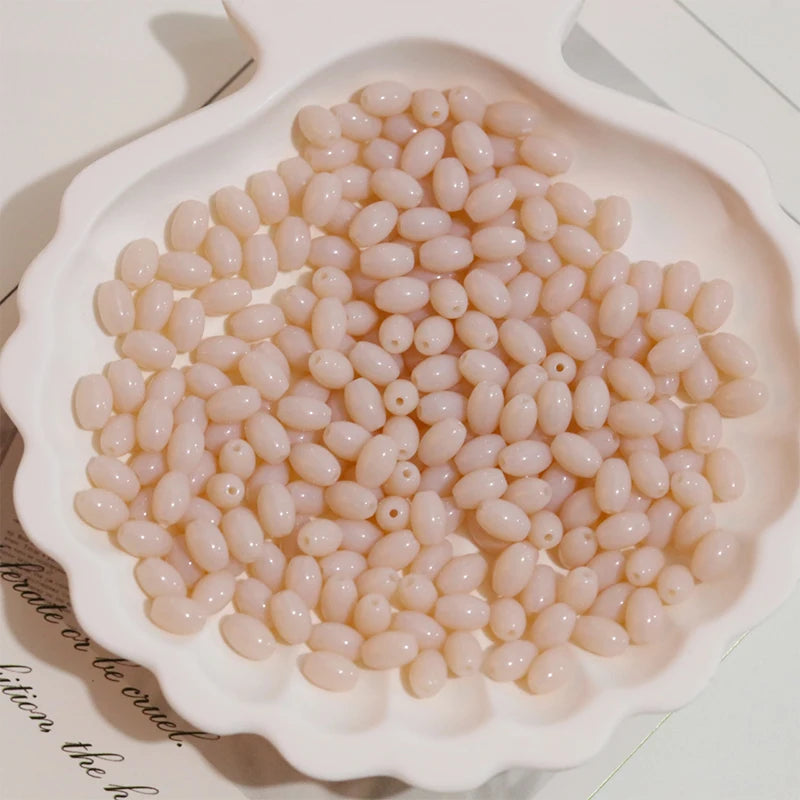 A pile of pale pink oval glass rice grain beads for jewelry making displayed in a white dish.