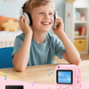 A young boy is smiling while using a pink instant print camera with headphones.