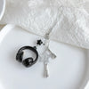 Silver beaded wing cross phone lanyard keychain with a black earbud charm on a white background
