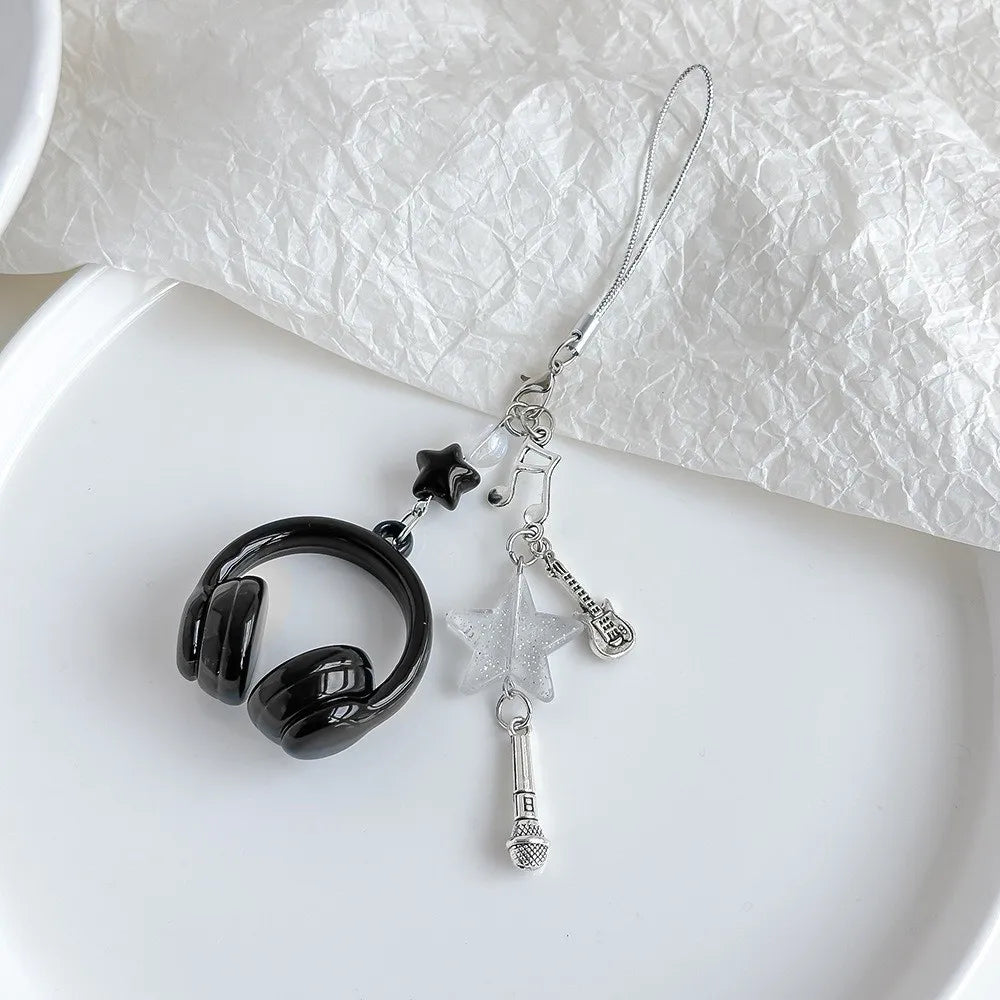 Silver beaded wing cross phone lanyard keychain with a black earbud charm on a white background