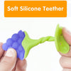 A hand holds a soft silicone fruit-shaped baby teether with purple and lime green silicone parts.