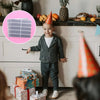 A smiling toddler boy wearing a gray outfit stands in front of a cabinet with various items and colorful gift boxes.