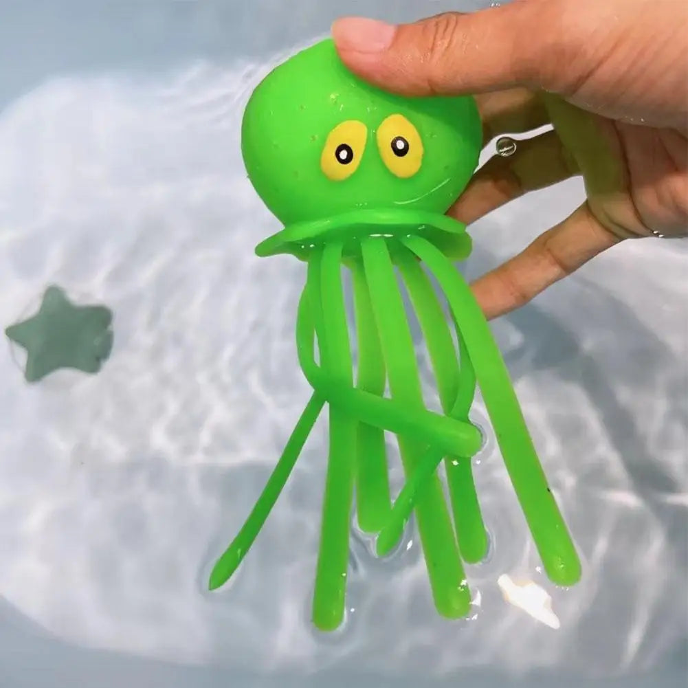 A bright green squeeze and soak octopus bath toy with yellow eyes is being held over water.