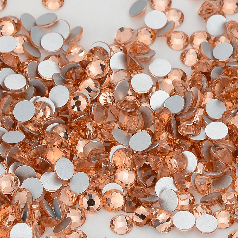 A close-up of various flatback glass crystal rhinestones in shades of peach and silver.