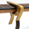 A brass aluminum alloy quick-change guitar capo is shown clamped onto the fretboard of a stringed instrument.