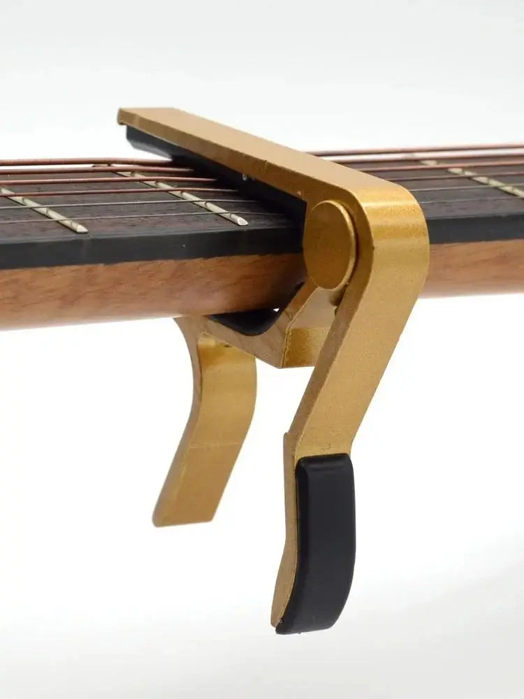 A brass aluminum alloy quick-change guitar capo is shown clamped onto the fretboard of a stringed instrument.