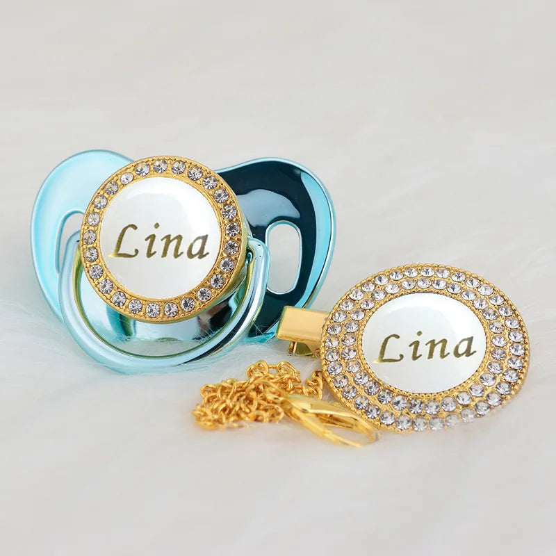 A gold and white bling pacifier clip featuring the name Lina on a light blue silicone ring.