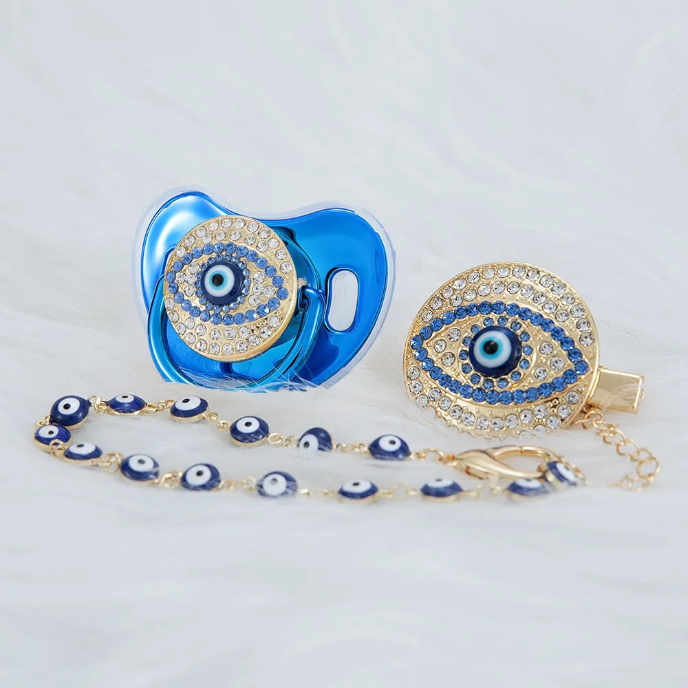 A set of blue pacifiers and clips featuring gold-toned evil eye designs with blue and white accents.