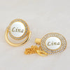 Gold pacifier clip with a circular nameplate engraved Lina and surrounded by white stones