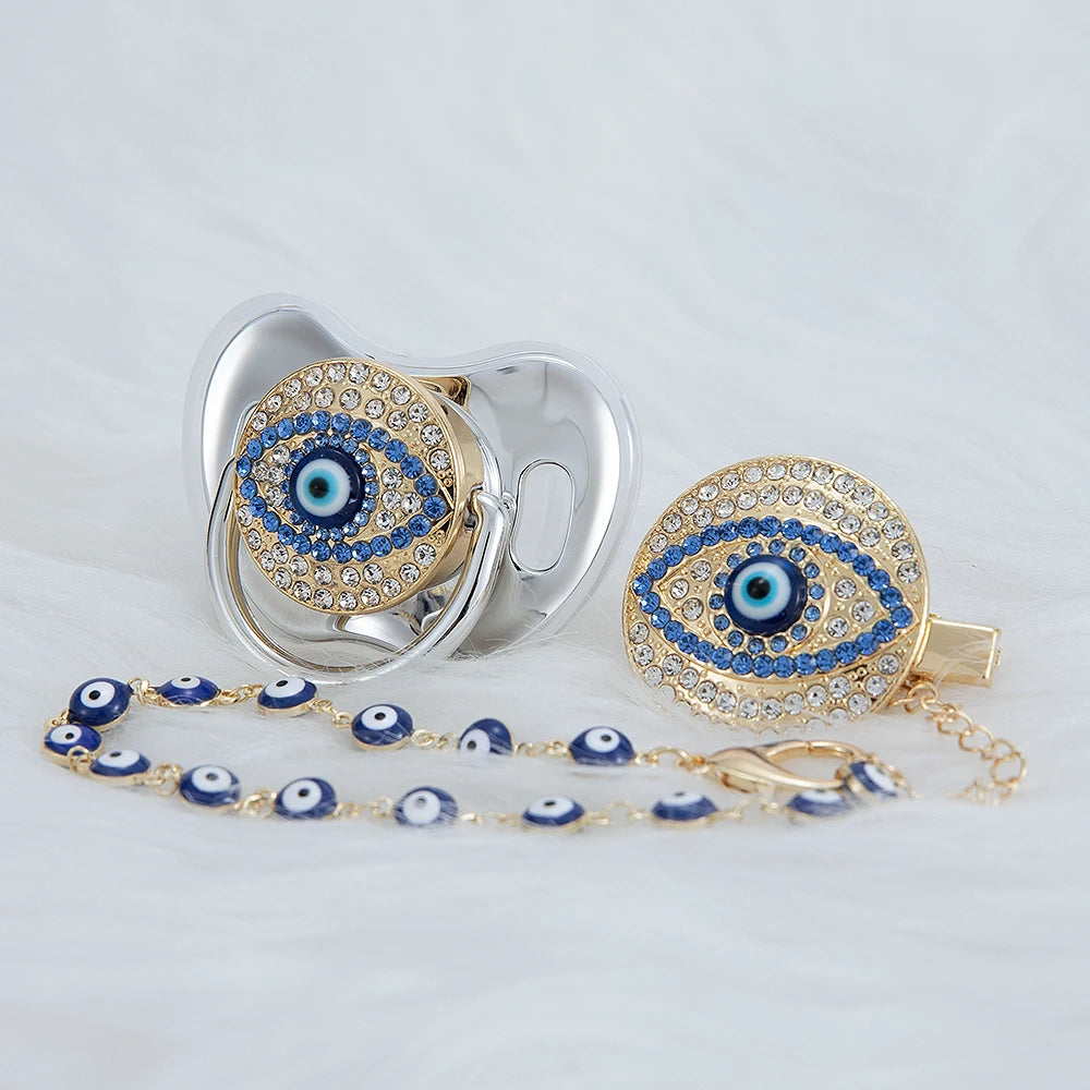 A set of silver and gold jewelry featuring an evil eye design, including a pacifier and clip.