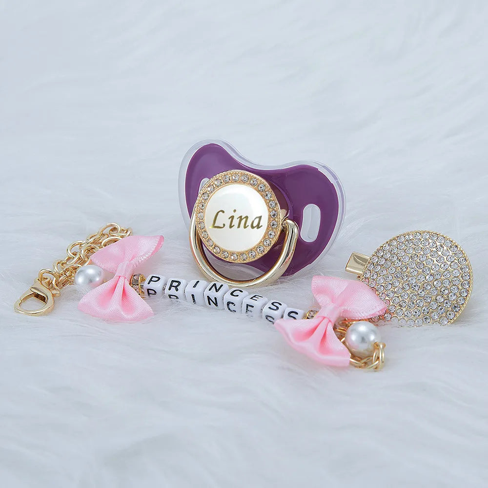 A personalized crystal pacifier with a clip featuring the name Lina and a matching pink ribbon and pearl accents.