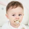 A close-up photo of a baby wearing a personalized crystal pacifier with a matching clip.