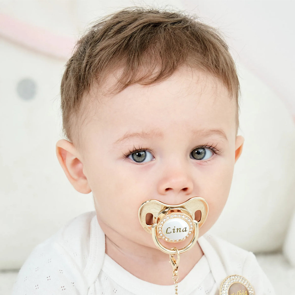 A close-up photo of a baby wearing a personalized crystal pacifier with a matching clip.