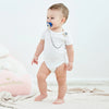 A baby wearing a white outfit with a blue evil eye pacifier and clip set