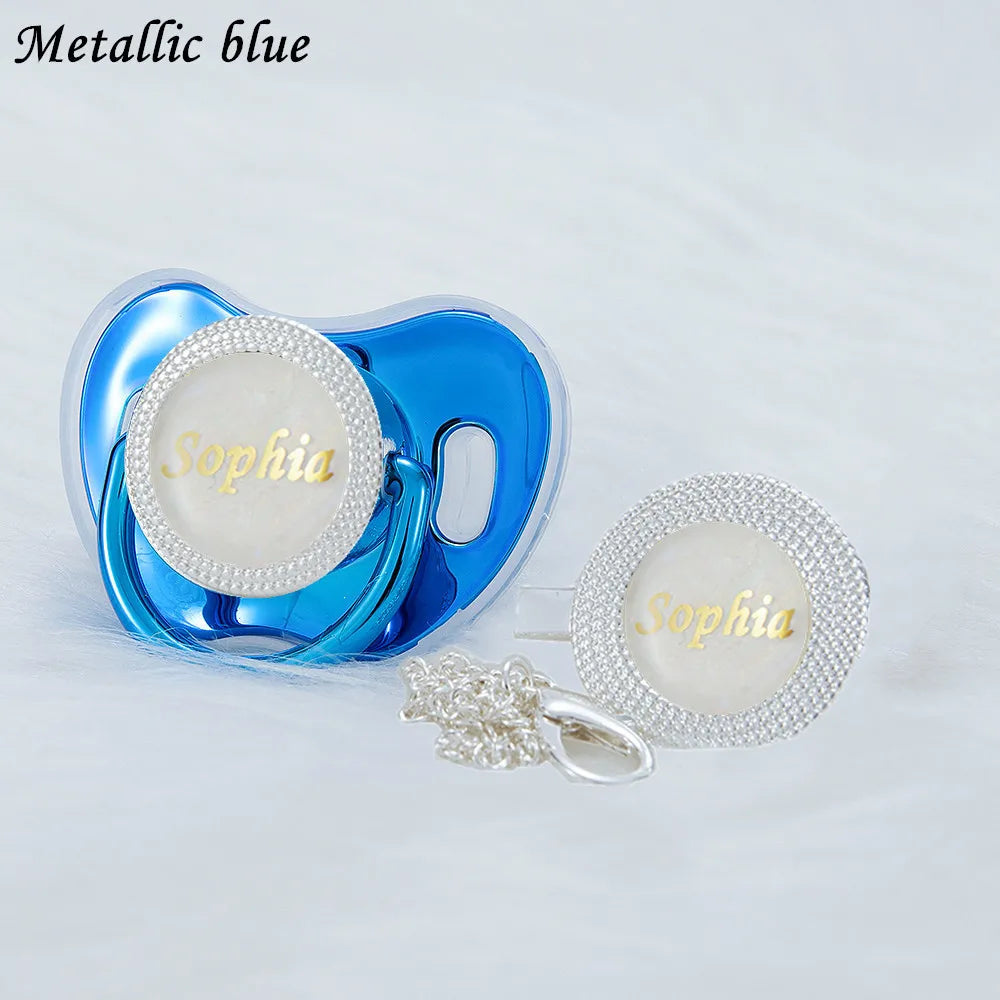 A metallic blue pacifier and clip set featuring a clear silicone body and a white rhinestone nameplate
