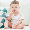 A baby is holding a personalized crystal pacifier and clip gift set while sitting on a light-colored couch cushion.
