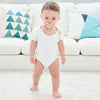 A baby wearing a white onesie with a crystal pacifier and clip on, sitting on a white sofa.