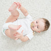 A baby lying on a white fluffy surface holding a personalized crystal pacifier and clip gift set