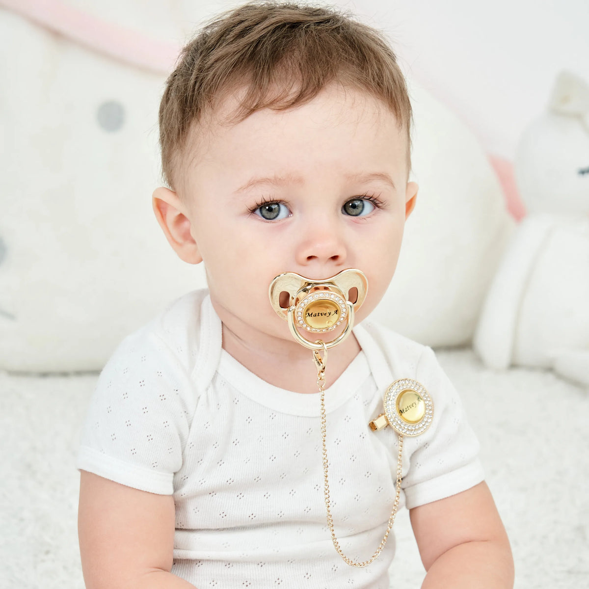A baby is shown holding a personalized crystal pacifier and clip gift set.