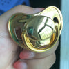 A hand holds a gold-colored silicone pacifier with a clear gemstone detail.