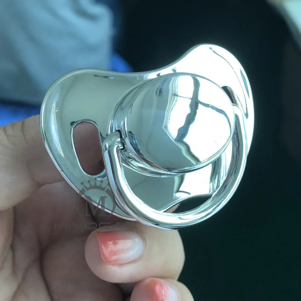 A hand holds a shiny silver silicone pacifier with a rounded, smooth design.