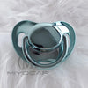 A clear silicone pacifier with a rounded top and surrounding ring, resting on white fluffy material.