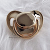 A gold-toned silicone pacifier with a smooth, rounded top and surrounding ring.