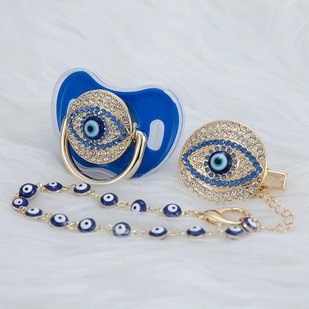 A set of blue silicone pacifiers and a gold-toned evil eye clip with blue and gold accents.