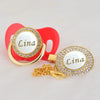 Gold and white bling pacifier clip with the name Lina on a red background