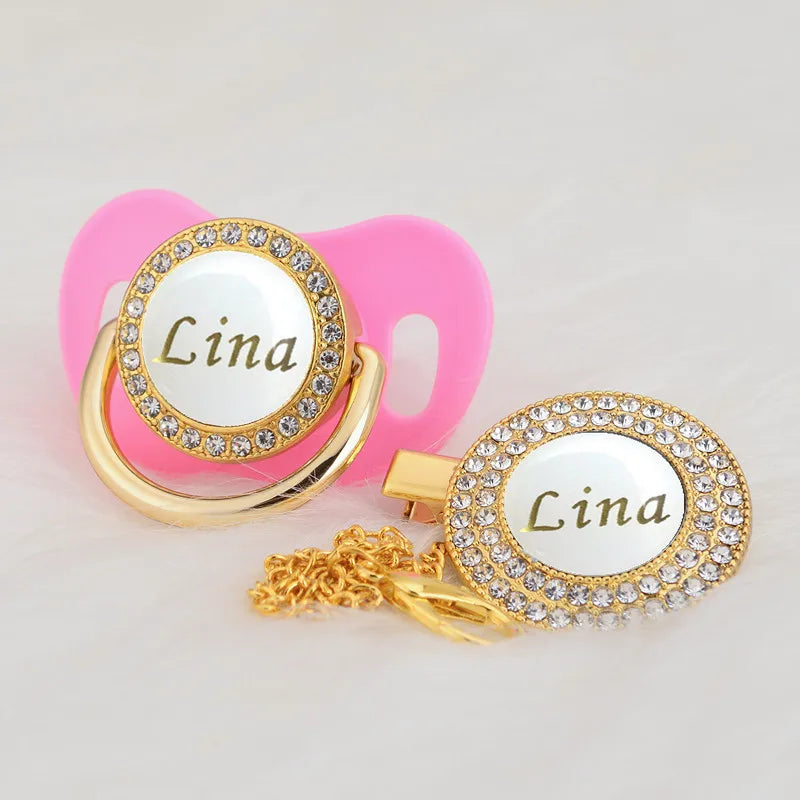 Gold and white bling pacifier clip with a pink silicone holder and a gold charm featuring the name Lina
