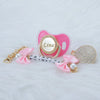 Pink crystal pacifier with a gold clip and pink ribbon, featuring the name Lina.
