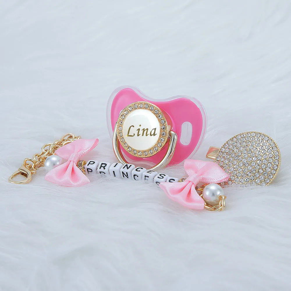 Pink crystal pacifier with a gold clip and pink ribbon, featuring the name Lina.