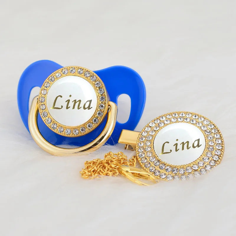 Gold and white bling pacifier clip featuring the name Lina on a blue silicone ring.
