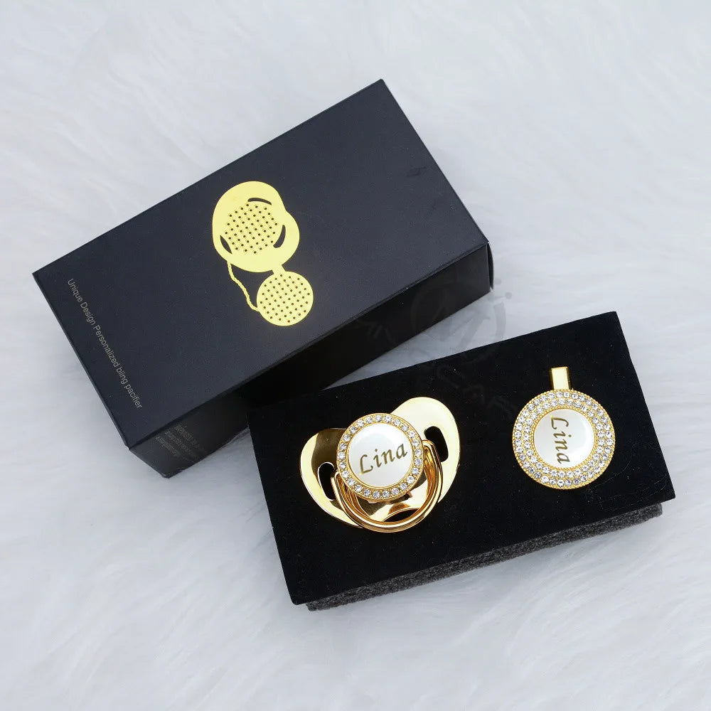A black box containing a personalized crystal pacifier and matching clip with gold accents.